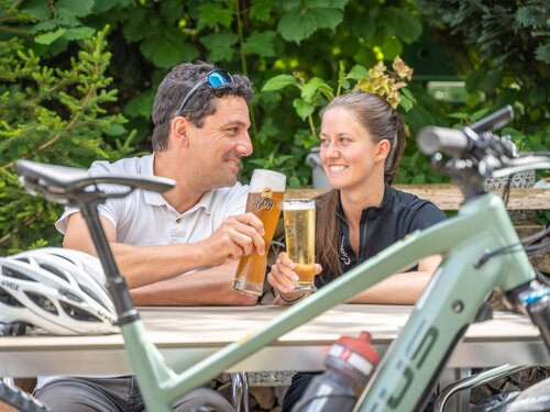 Ein Mann und eine Frau stoßen mit Bier an, während sie vor einem Fahrrad stehen.