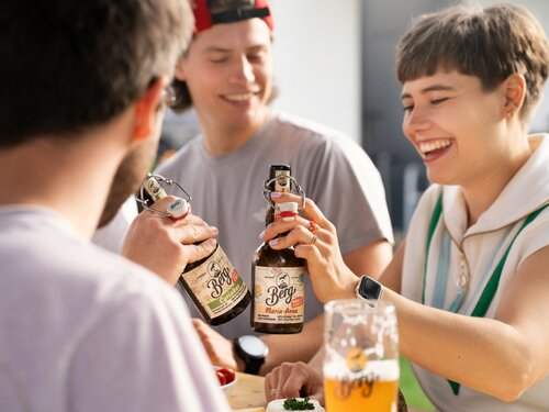 Eine Gruppe von Menschen sitzt um einen Tisch, umgeben von Bierflaschen, und genießt gemeinsam die Zeit.