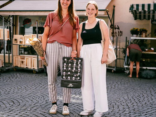 Zwei Frauen stehen in einer Fußgängerzone und halten eine Tasche.