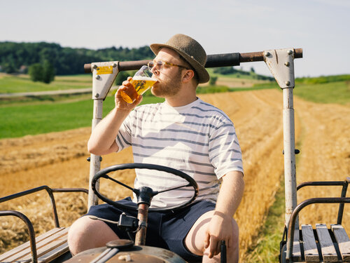 Bauer auf Traktor mit Bier auf abgeerntetem Gerstenfeld