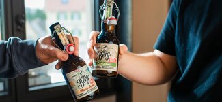 Zwei Personen halten Bierflaschen vor einem Fenster und genießen gemeinsam den Moment.